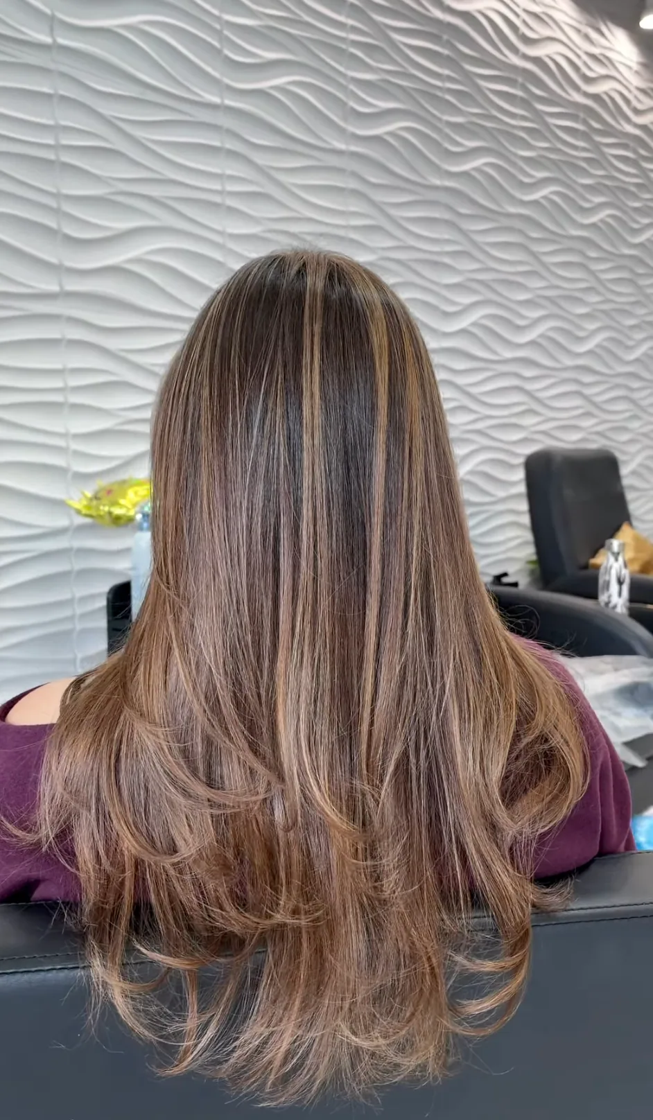 Long layered brunette hair with soft highlights, seen from behind in the salon