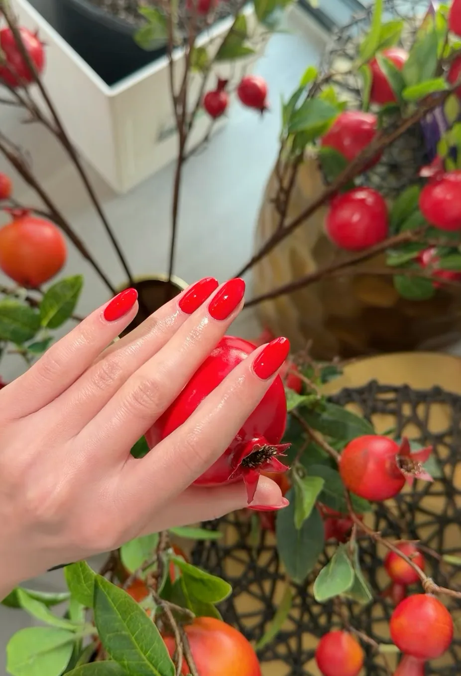 Glossy red almond manicure holding a pomegranate among red berries